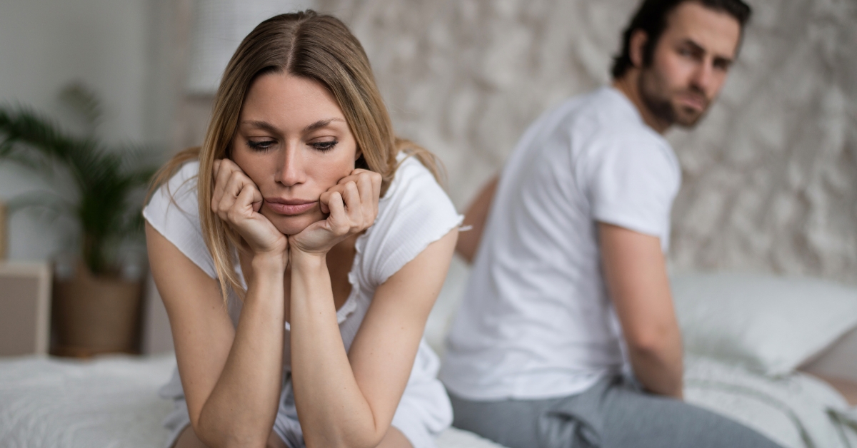 Couple lying in bed back to back looking distant and unhappy, representing relationship stress and low libido