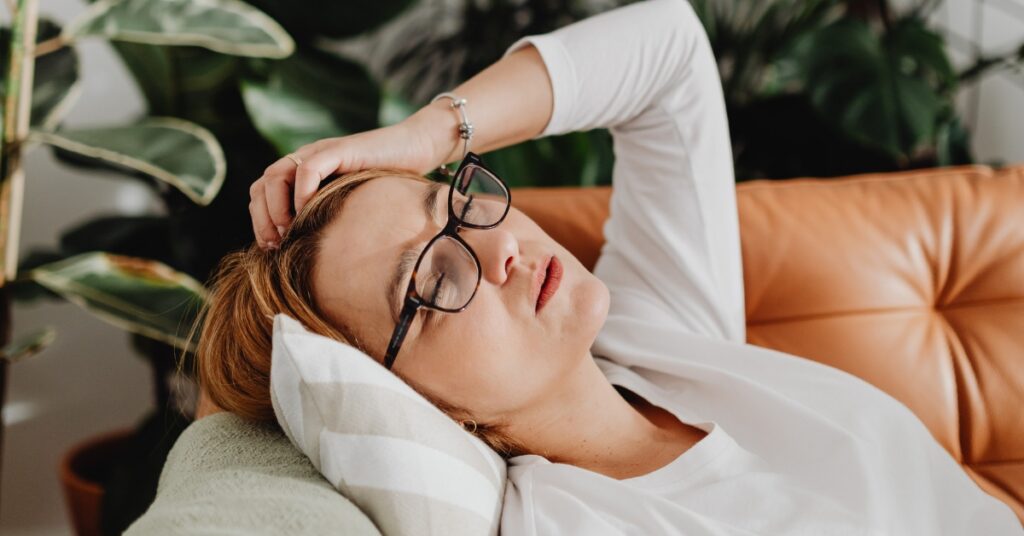 Woman sitting on a couch looking tired and low energy, representing fatigue related to stress or hormone imbalance
