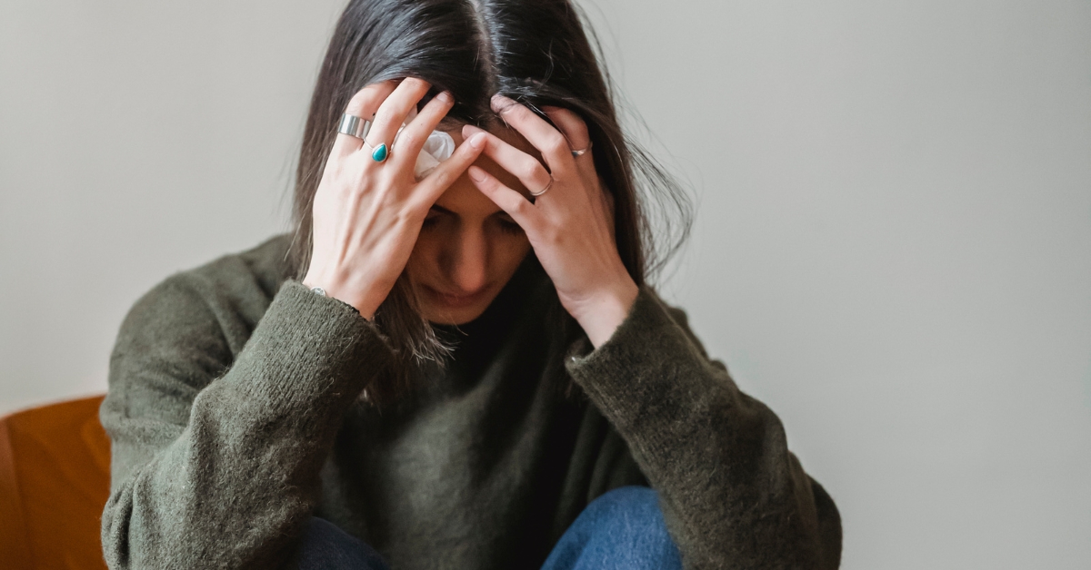 Woman sitting alone looking anxious and overwhelmed, representing hormone-related anxiety and stress