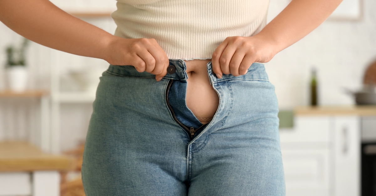Woman struggling to button tight jeans during menopause-related weight changes
