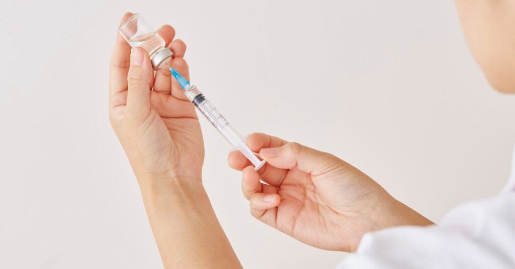 Person drawing prescribed medication from a vial into a syringe.