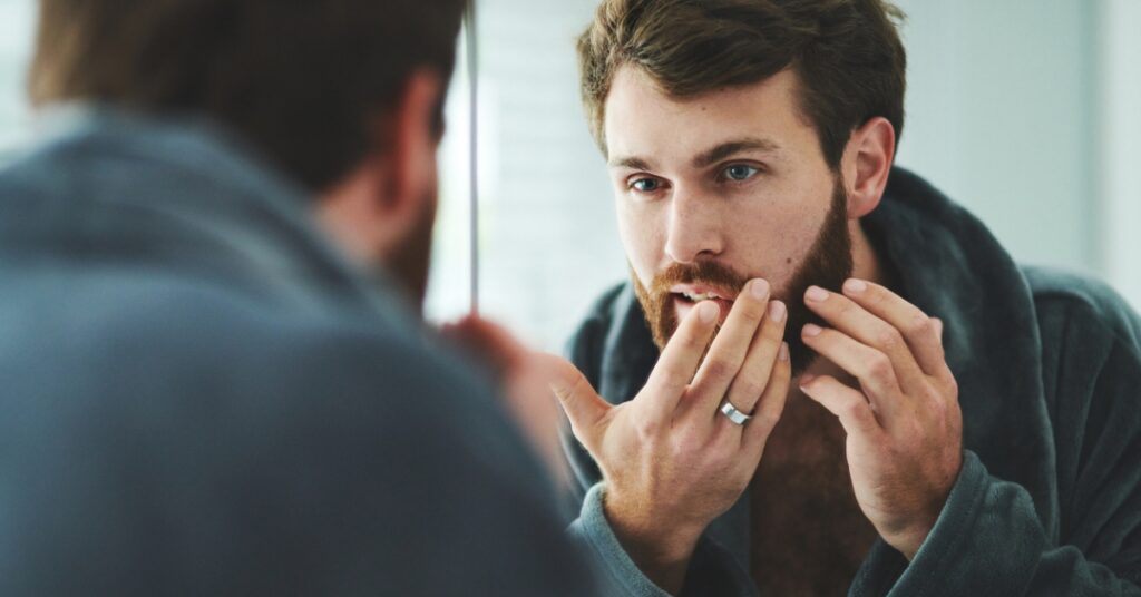 Man looking in the mirror while checking his skin for acne