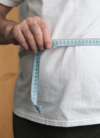 Fat mature man measuring his belly with measurement tape standing in the living room. Problem with overweight, bad health and dieting concept