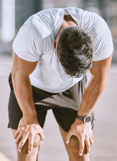 Tired man resting after fitness run, taking a break from cardio training and doing wellness exercise on the road in the urban city. Exhausted and fit sports person doing routine workout in street