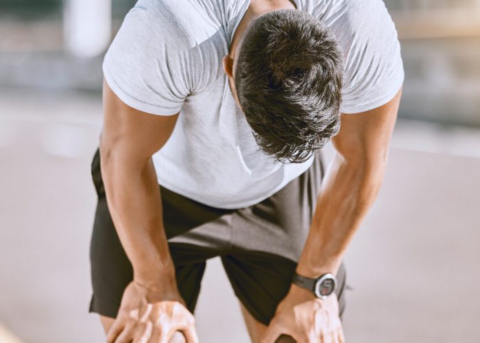 Tired man resting after fitness run, taking a break from cardio training and doing wellness exercise on the road in the urban city. Exhausted and fit sports person doing routine workout in street