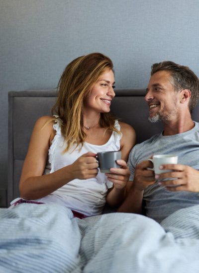 Happy couple communicating while having coffee during morning time in a bed. Copy space.