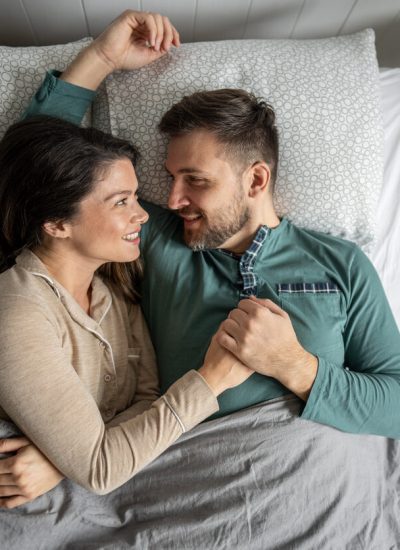High angle view of a loving couple lying in bed, holding hands and looking at each other with affection, enjoying a peaceful moment of intimacy in their bedroom