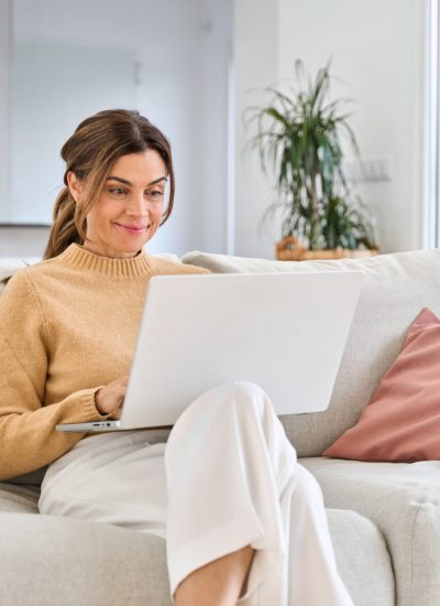 Women in her 50's looking at her laptop while sitting on a couch